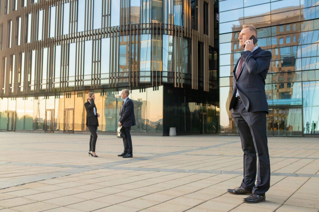 serious confident businessman wearing office suit talking mobile phone outdoors businesspeople city building glass facade background copy space business communication concept scaled 1